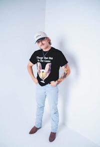 a man wearing a t - shirt and jeans standing in front of a white wall